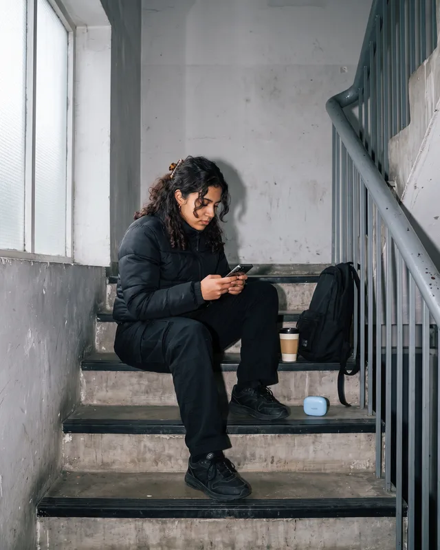 She sits on the stairs with her phone, the case on the step beside her